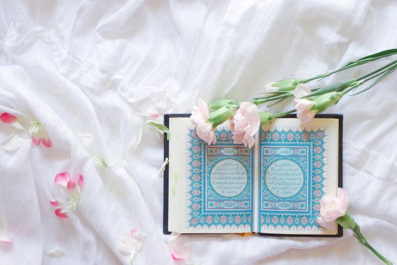 A picture of a beautiful Quran on top of pristine white sheet, decorated with real flowers.